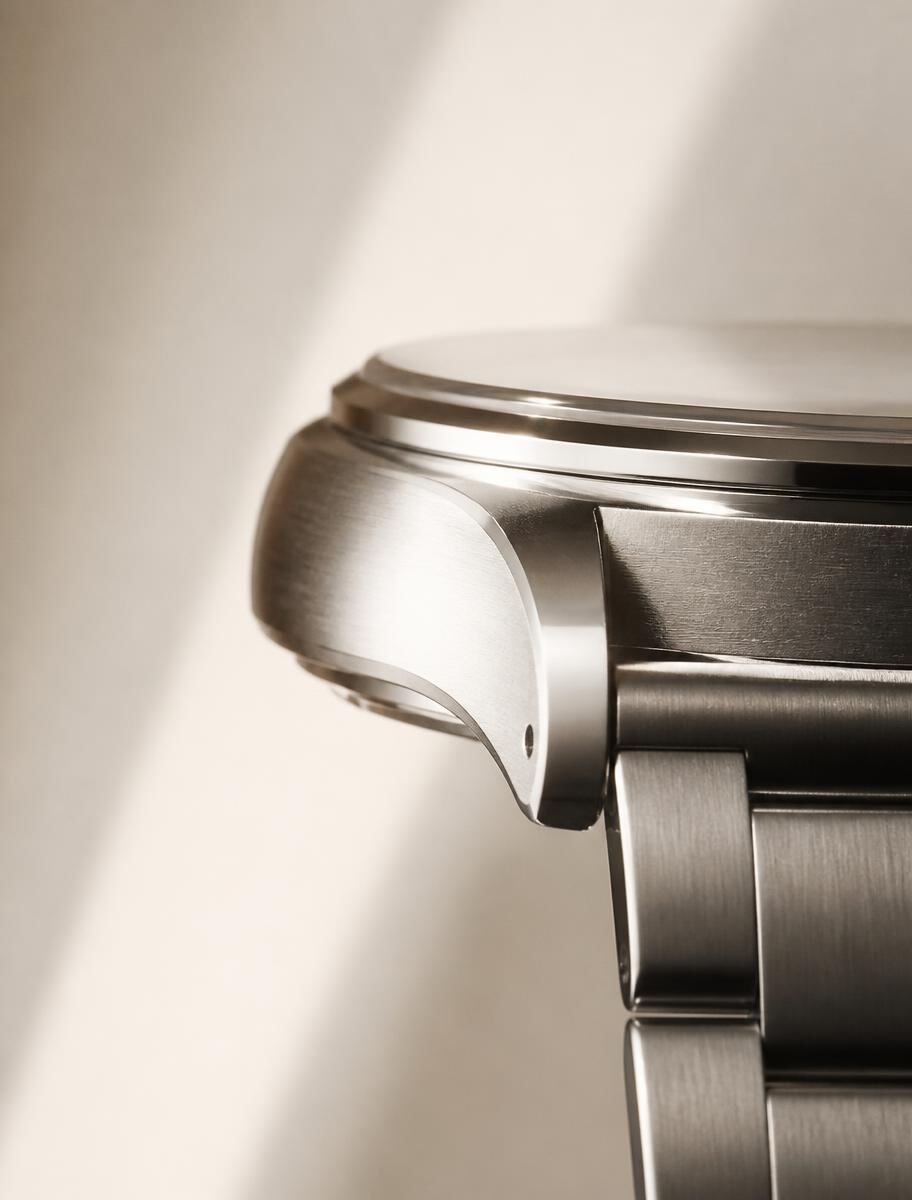 The polished side profile of a steel watch case resting on a plain surface